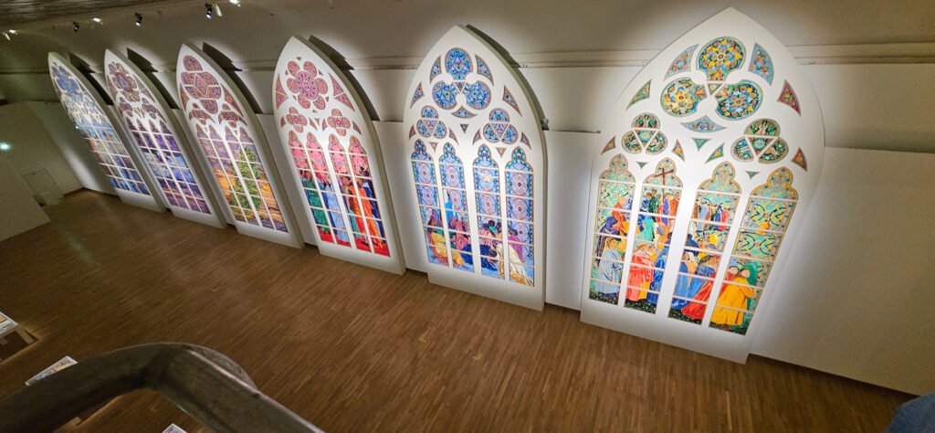 Panneaux en forme de baies gothiques éclairés dans une galerie du Grand Palais.