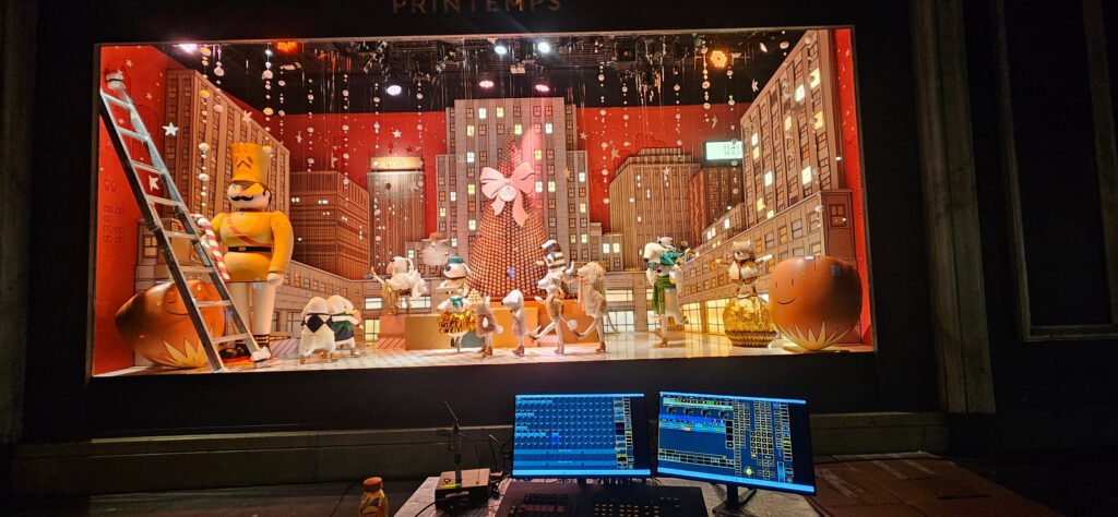 Vitrine de Noël du Printemps éclairée, avec console de programmation au premier plan.
