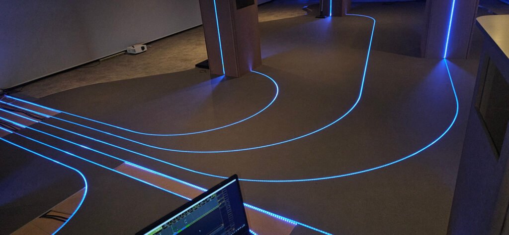 Lignes lumineuses bleues intégrées au sol et aux parois d’un espace interactif.